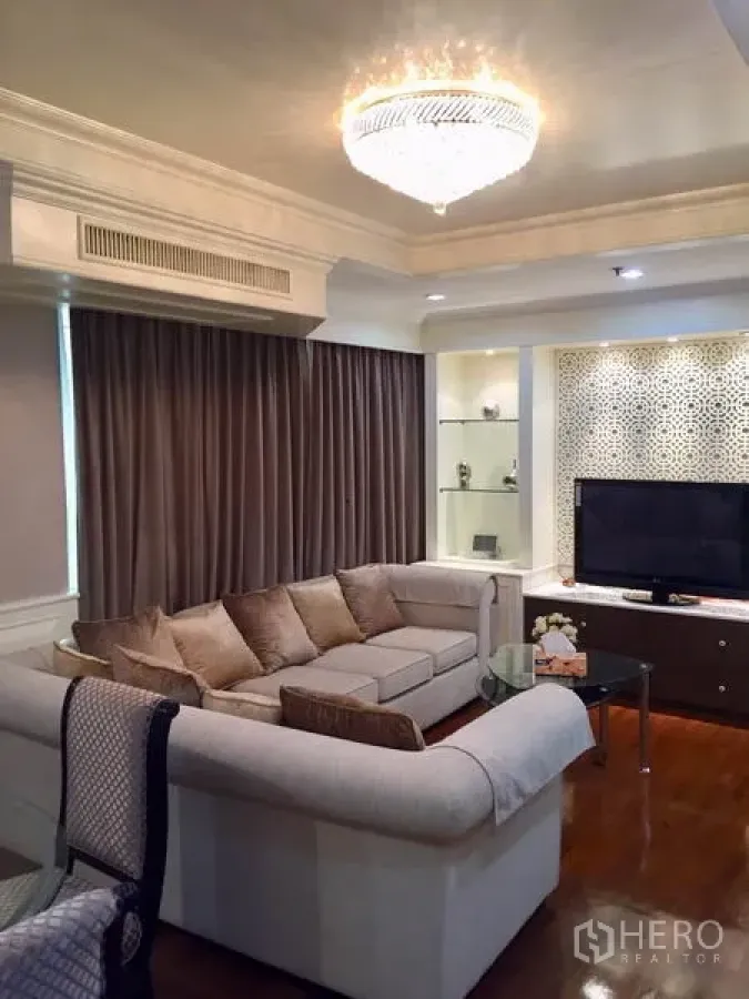 Condominium for sale in Watthana, Bangkok - Living area with sectional sofa facing TV console, display shelves and chandelier.