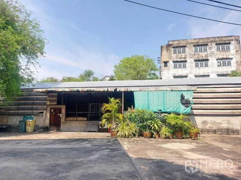 货栈 出租在Min Buri, Bangkok - 单层附属建筑，前有盆栽绿植与硬化作业区