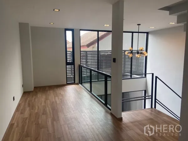 Townhouse for rent in Huai Khwang, Bangkok - Upper lounge with wood floors and floor-to-ceiling windows beside the void.