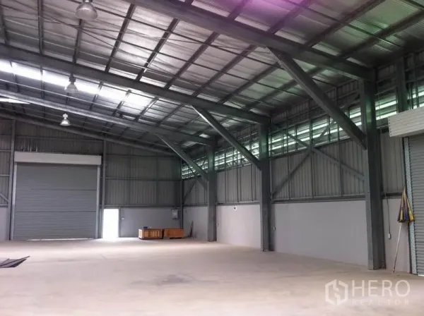 Warehouse for rent in Sai Mai, Bangkok - Spacious warehouse interior in Sai Mai, Bangkok with high steel truss ceiling, skylight strips, concrete floor and large roller shutter door.