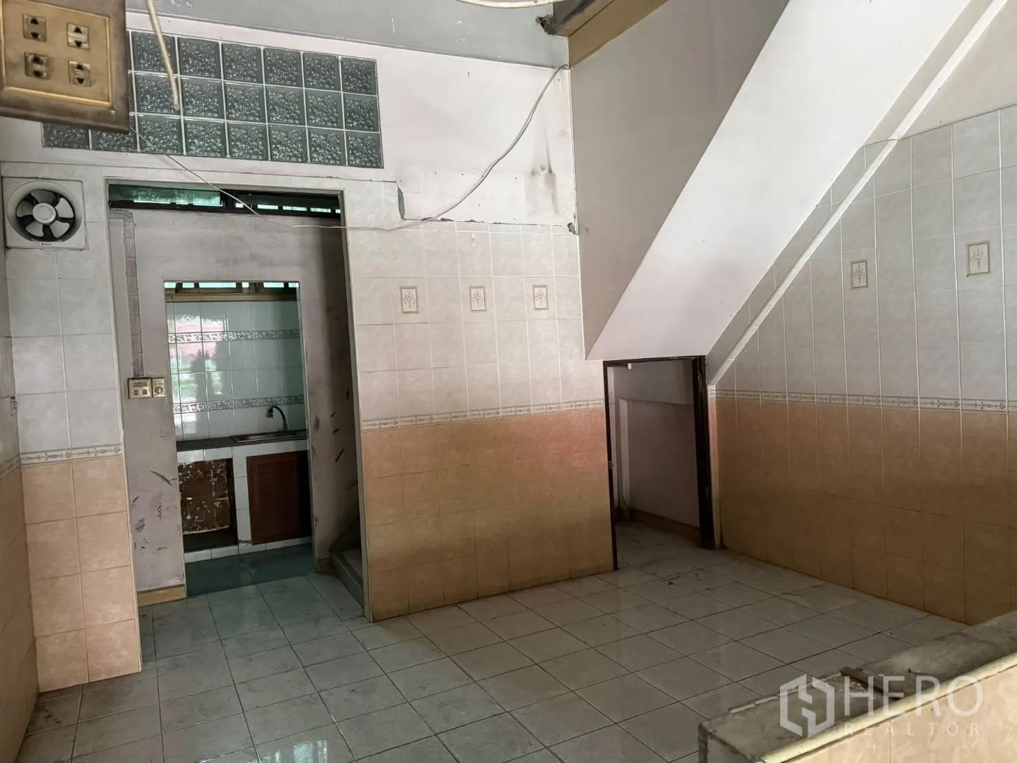 Shophouse for rent in Khlong Toei, Bangkok - Tiled rear area with a sink, ventilation fan, and space beneath the stairs.