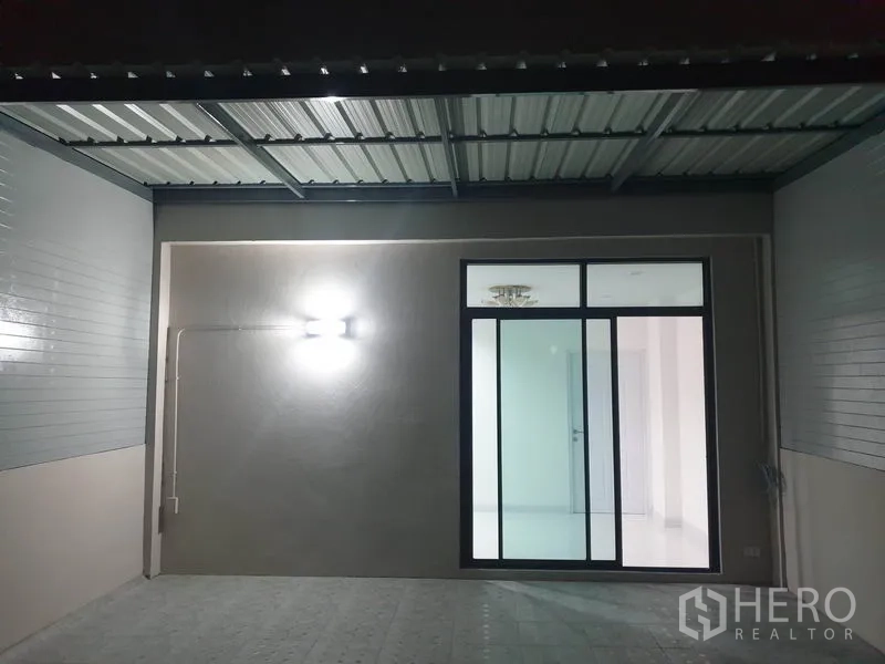 Home Office for rent in Wang Thonglang, Bangkok - Covered carport or terrace with wall light and sliding glass entrance at night.