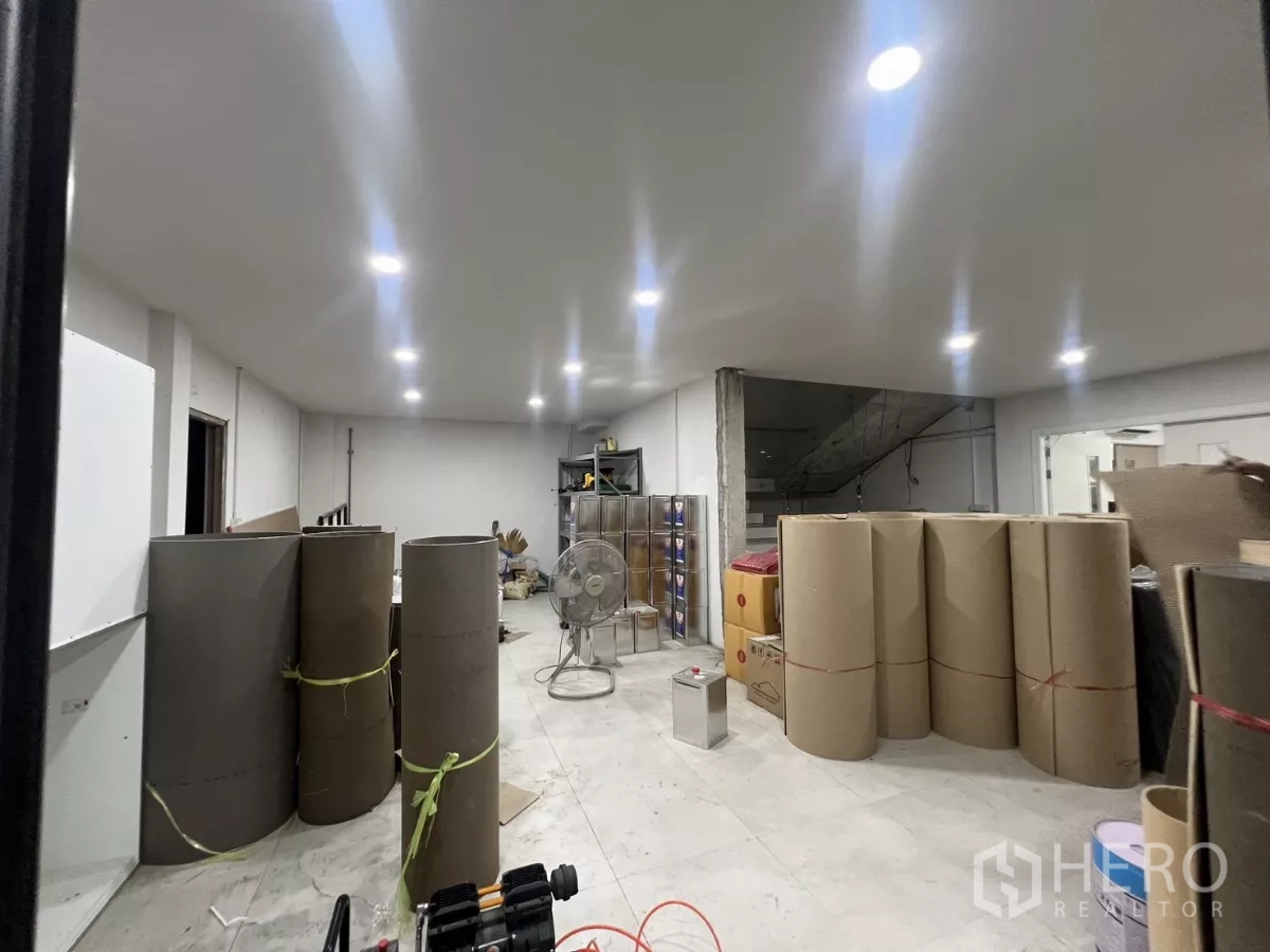 Warehouse for rent or sale in Lat Krabang, Bangkok - Bright ground-floor room with recessed LED lights and large rolls of packaging materials.