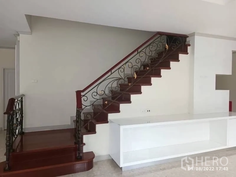 Detached House for sale in Prawet, Bangkok - Interior staircase with polished wood steps and wrought-iron railing beside a white built-in console.
