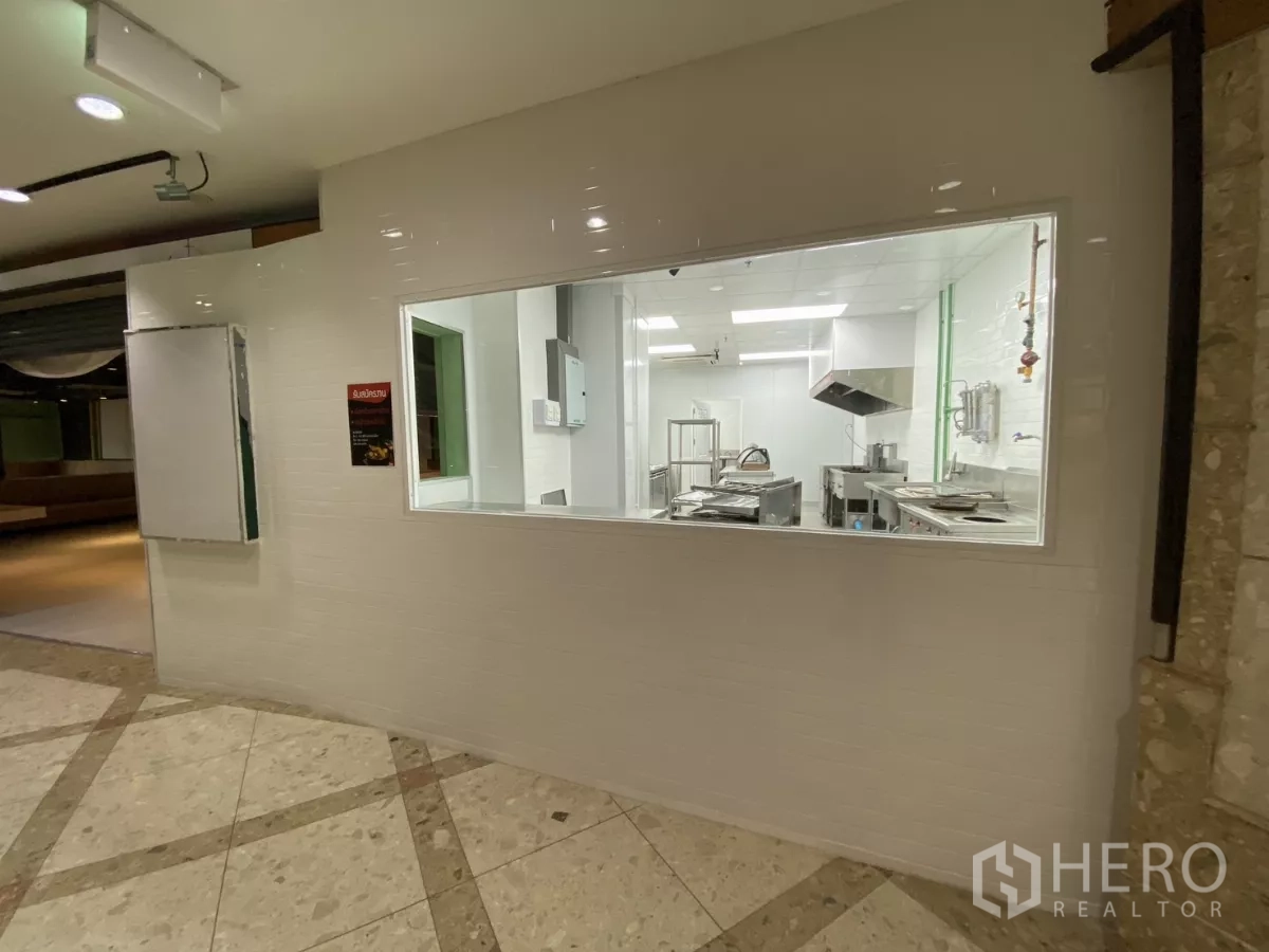 Retail Space for rent - Viewing window into a commercial kitchen with white tiles and stainless-steel equipment.