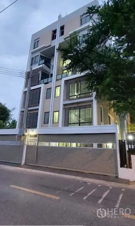 Home Office for rent in Huai Khwang, Bangkok - Street view of a contemporary home office facade with illuminated windows and a perimeter wall.