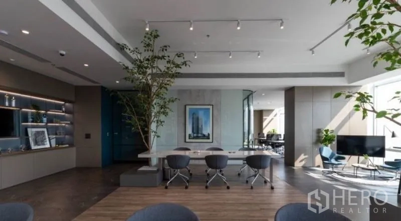 Office Space for rent - Fitted collaborative area with long table, indoor greenery, lounge seating and track lighting.