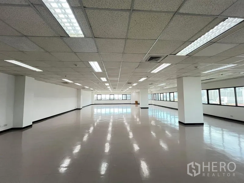 Office Space for rent or sale - Empty office space with polished flooring, structural columns and full‑length windows on two sides providing natural light.