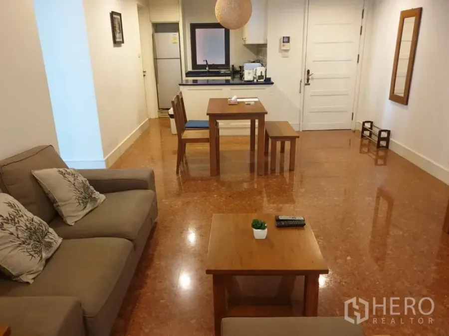 Condominium for rent or sale in Khlong Toei, Bangkok - Open-plan living and dining area with sofa, wooden tables and a compact kitchen in a modern Bangkok condo.