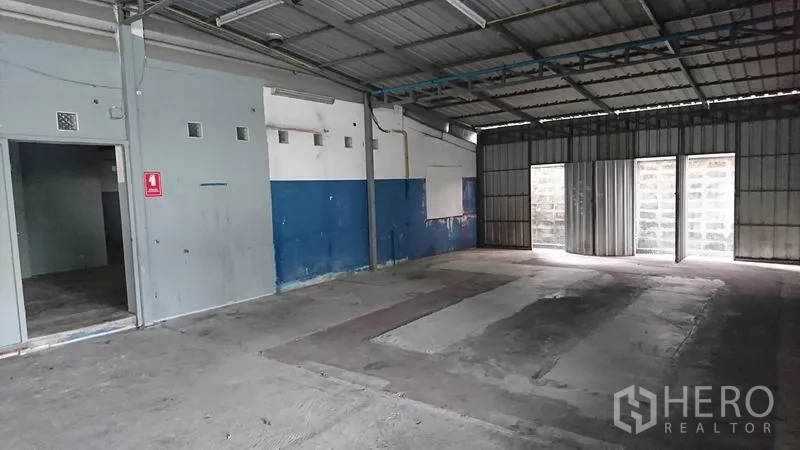 Warehouse for rent in Lak Si, Bangkok - Open-plan warehouse interior with concrete floor, blue accent wall, and sliding metal doors.