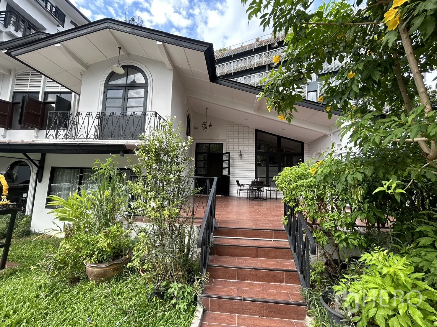Retail Space for rent in Bangkok - White low-rise retail building with arched window, garden frontage and tiled steps leading to a covered terrace.