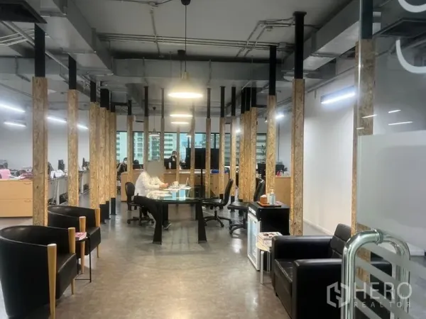 Office Space for rent - Collaborative area featuring a round glass meeting table, pendant lights, wood-accent columns, and lounge chairs.