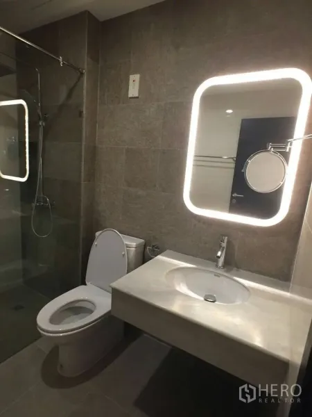 Townhouse for rent in Khlong Toei, Bangkok - Modern bathroom featuring LED backlit mirror, vanity sink, toilet, and glass-enclosed shower.