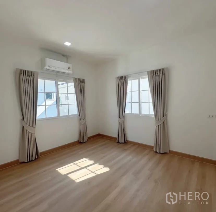 Detached House for rent in Mueang Samut Prakan, Samut Prakan - Spacious bedroom with two windows, curtains and a wall-mounted air conditioner.
