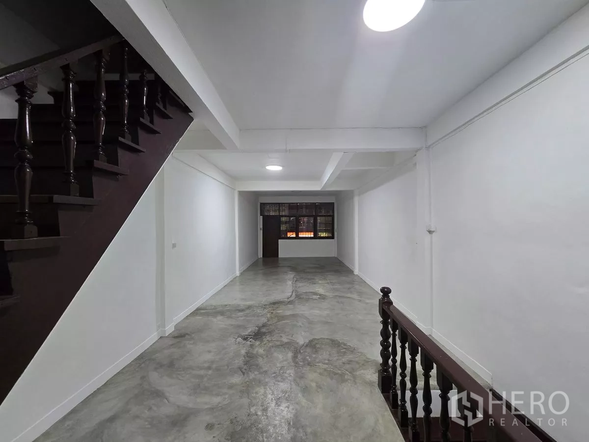 Shophouse for rent in Watthana, Bangkok - Interior view showing a wooden staircase and spacious concrete‑floored level.