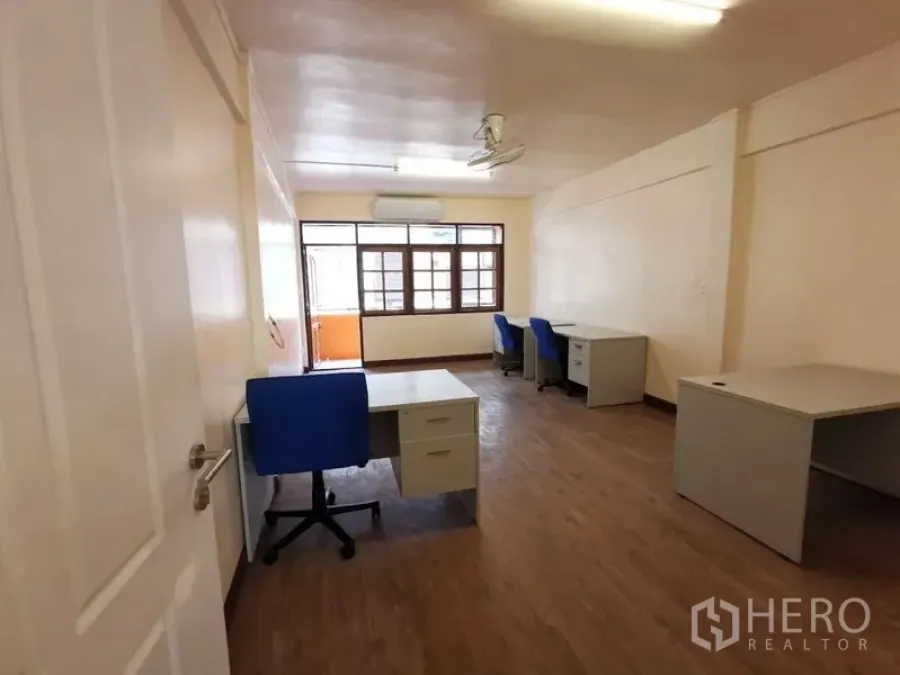 Townhouse for rent in Watthana, Bangkok - Work-ready room with multiple desks, blue chairs, wood floors, and a small front balcony.
