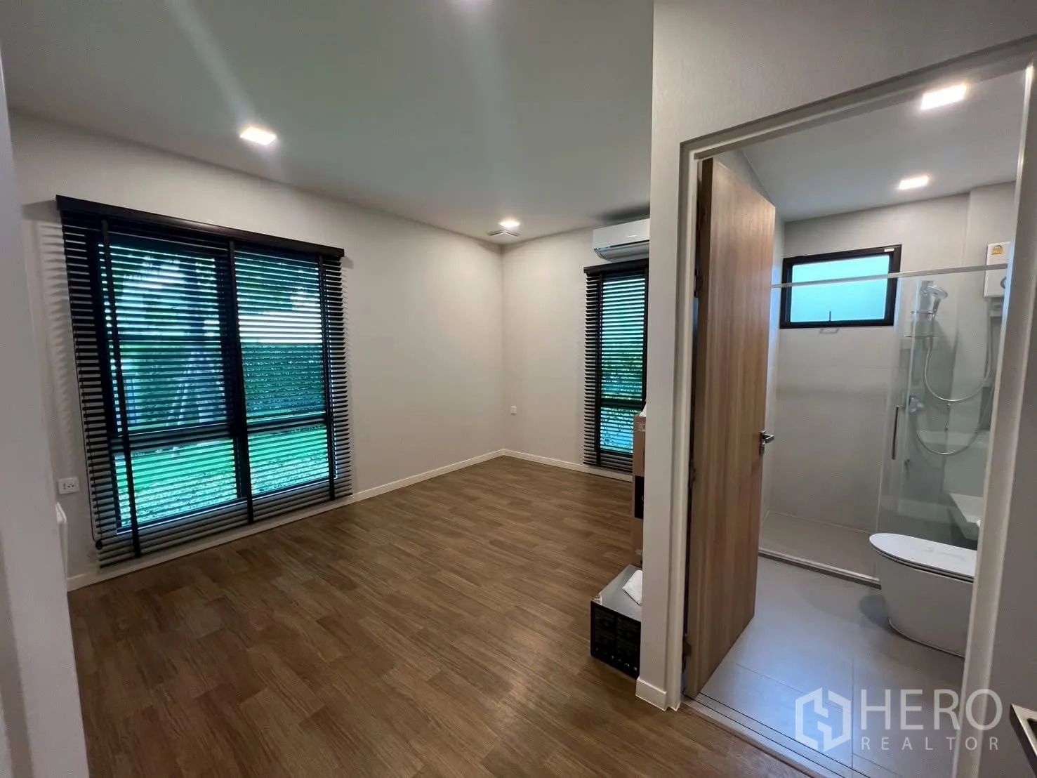 Detached House for rent in Samut Prakan - Ensuite bedroom with wood floors and garden-view windows.
