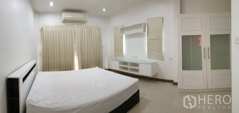 Detached House for rent in Khlong Toei, Bangkok - Spacious bedroom with bed, built-in shelving, wardrobe and full-length curtains.