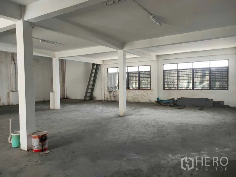 店屋 出租在Watthana, Bangkok - 明亮开阔楼层，水泥地面、大窗与靠墙的梯子通道。
