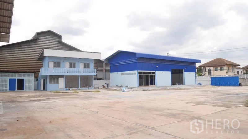 Factory for rent in Khlong Sam Wa, Bangkok - Factory compound showing a blue-roof warehouse, two-storey office building and expansive paved yard.