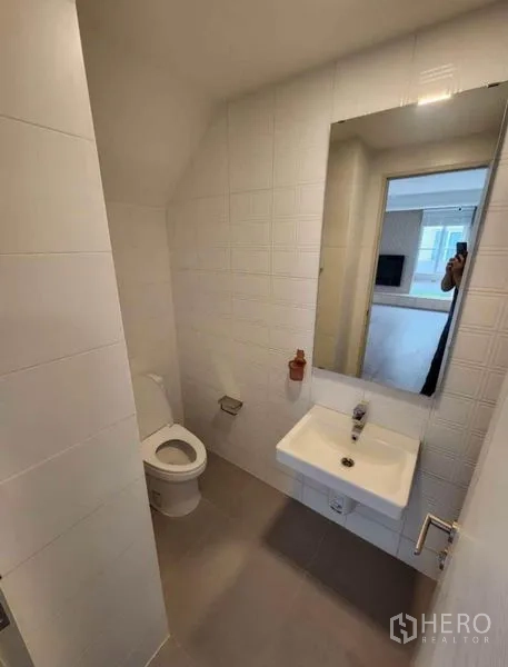 Detached House for rent in Prawet, Bangkok - Downstairs powder room with wall-mounted sink, mirror, and white tiled walls.