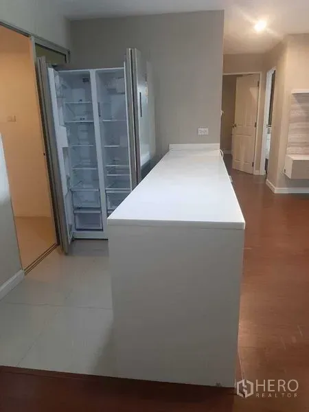 Condominium for rent or sale in Huai Khwang, Bangkok - Hallway view with a long white counter and an open double-door refrigerator.