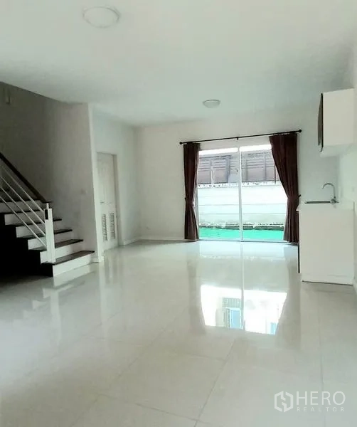 Townhouse for sale in Mueang Pathum Thani, Pathum Thani - Living room view to kitchenette and staircase, large sliders bringing natural light.