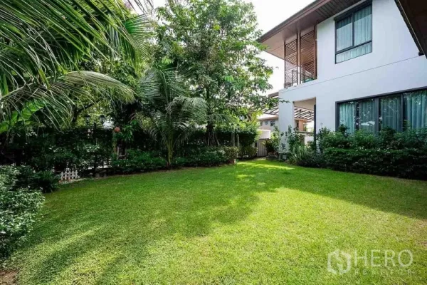 Detached House for sale in Prawet, Bangkok - Green garden with mature trees beside the white two-storey home.