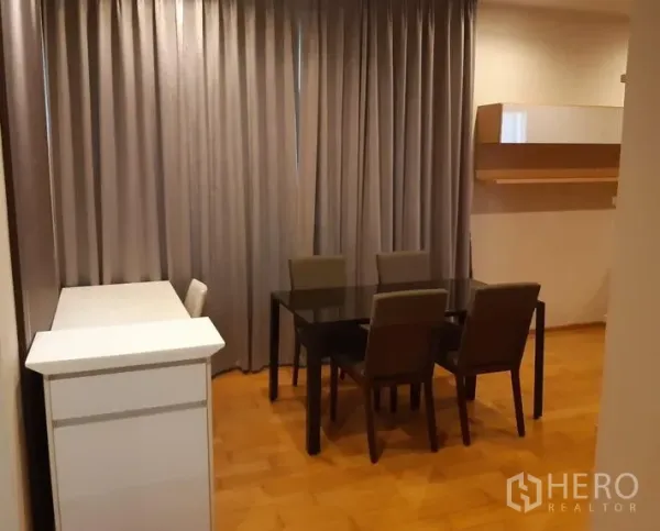 Condominium for rent in Khlong Toei, Bangkok - Four-seat dining area with glass-top table, fabric chairs, floor-to-ceiling curtains and wooden floor.