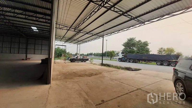 Warehouse for rent in Khlong Luang, Pathum Thani - Covered loading apron with steel canopy and wide driveway connecting to the main road, next to the warehouse interior.