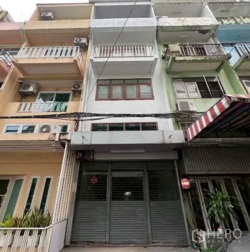 店屋 出租在Khlong Toei, Bangkok - 城市街巷中的店屋外立面，金属卷闸门与多层阳台。