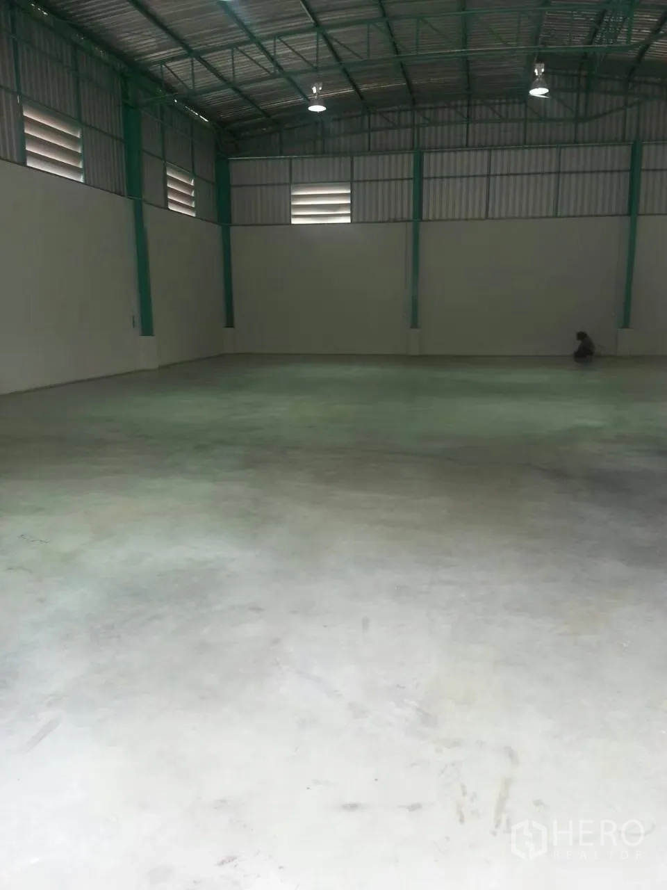 Warehouse for rent in Pathum Thani - Empty warehouse hall showing heavy-duty concrete slab floor, green steel frames and ventilated side windows.