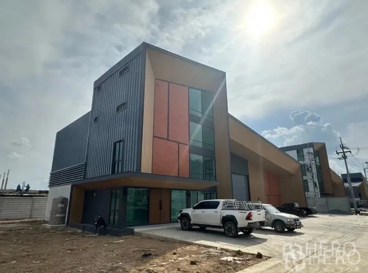 Warehouse for sale in Lam Luk Ka, Pathum Thani - Modern warehouse exterior with metal cladding, brick accents and front parking for vehicles.