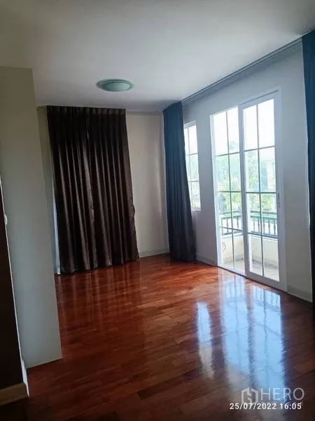 Detached House for sale in Prawet, Bangkok - Sunlit room with floor-to-ceiling glass doors and long curtains opening to a small balcony.