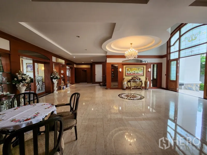 Detached House for rent in Prawet, Bangkok - Open lounge near the entrance with chandelier, tray ceiling and large arched windows for natural light.