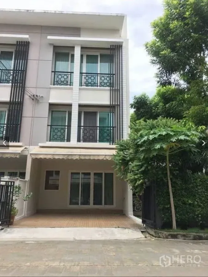 Townhouse for rent or sale in Suan Luang, Bangkok - Three-storey Suan Luang townhouse exterior with covered carport, balconies, and mature trees at the side.