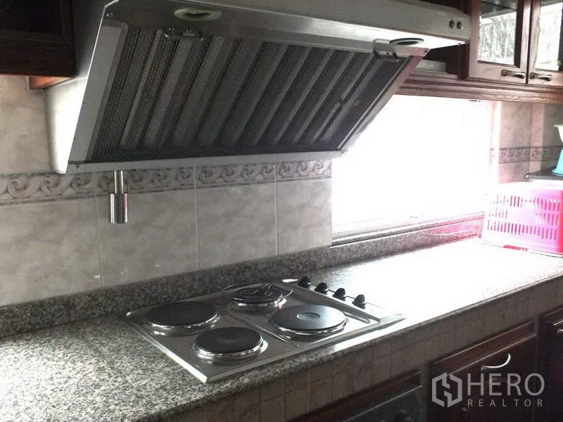 Detached House for rent in Bang Rak, Bangkok - Kitchen with granite countertop, electric cooktop and stainless range hood set beneath a bright window.