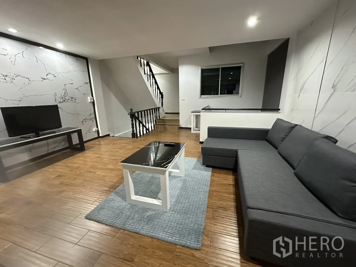 โฮมออฟฟิศ for rent in Khlong Toei, Bangkok - พื้นที่นั่งเล่นเปิดโล่ง โซฟาเข้ามุมสีเทา ชั้นวางทีวี และพื้นลายไม้