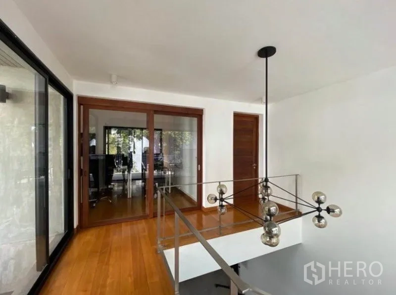 Townhouse for rent in Khlong Toei, Bangkok - Upper landing with glass balustrade, modern pendant light and sliding wooden doors.