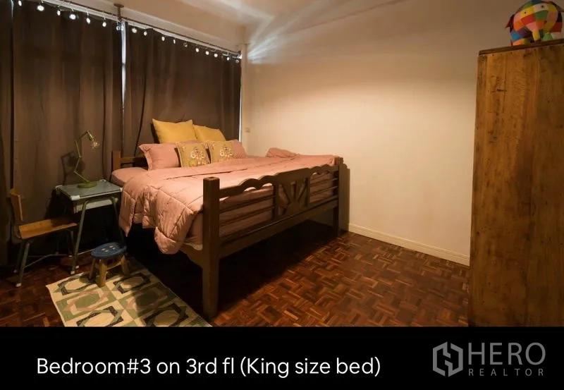 Townhouse for rent in Khlong Toei, Bangkok - Third-floor bedroom with king-size bed, dark curtains and wood parquet floors.