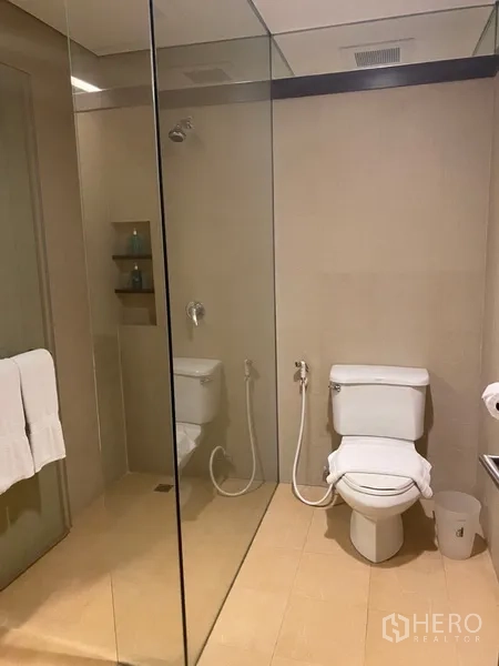 房间 出租在Khlong Toei, Bangkok - 现代浴室，设玻璃淋浴间、坐便器与浅色瓷砖。