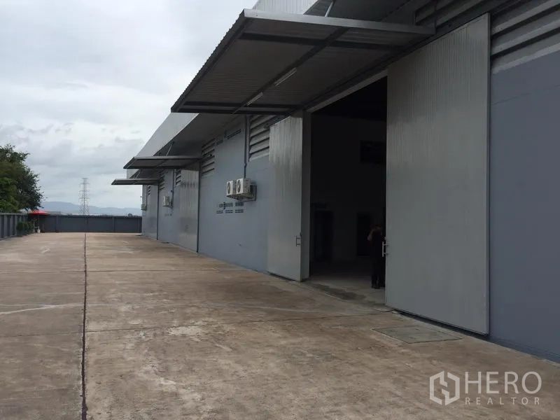 Warehouse for rent in Si Racha, Chon Buri - Exterior loading area with wide sliding metal doors, canopies and a concrete driveway for trucks.