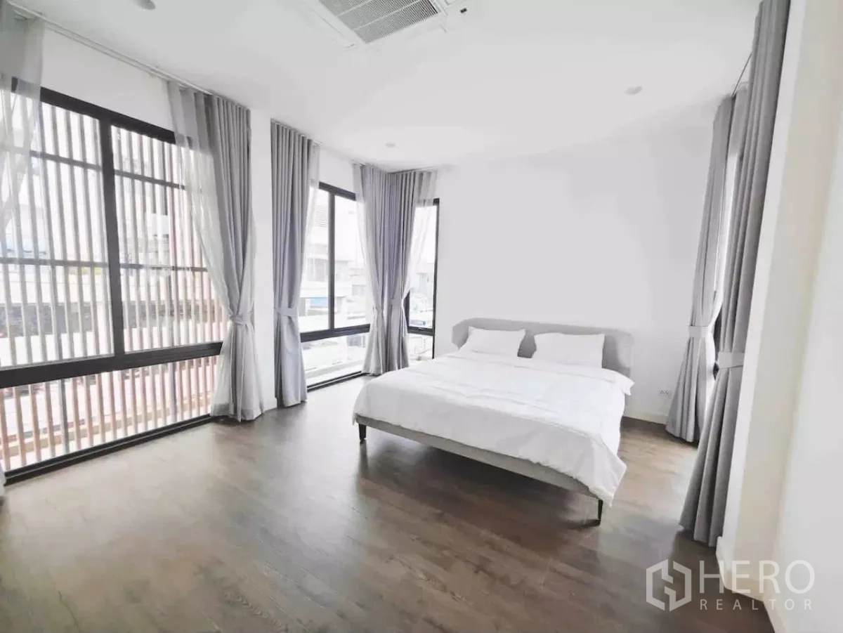 Detached House for rent in Phaya Thai, Bangkok - Sunlit bedroom with wraparound windows, grey drapes and dark wood flooring.