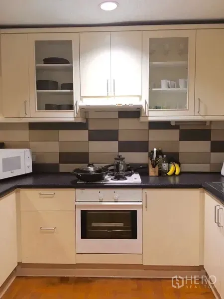 Condominium for rent in Pathum Wan, Bangkok - U-shaped kitchen with white cabinets, tiled backsplash, oven, microwave, and ample counter space.