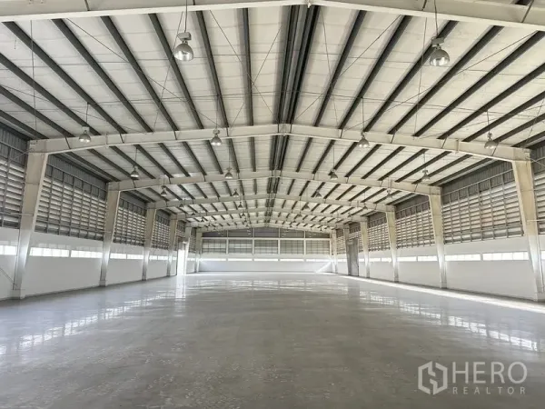 Factory for rent in Phra Nakhon Si Ayutthaya - Expansive warehouse interior with high steel truss roof, polished concrete floor, and louvered ventilation.