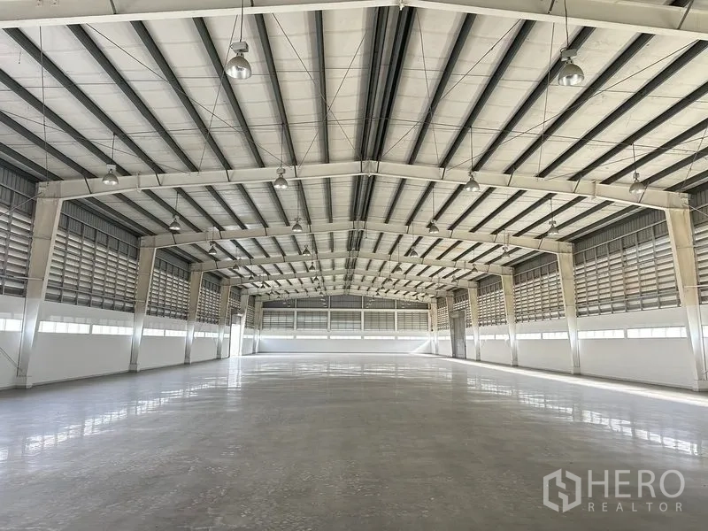 Factory for rent in Phra Nakhon Si Ayutthaya - Expansive warehouse interior with high steel truss roof, polished concrete floor, and louvered ventilation.