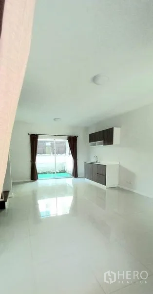 Townhouse for sale in Mueang Pathum Thani, Pathum Thani - Open-plan living area with glossy white tiles and rear sliding doors to the garden.