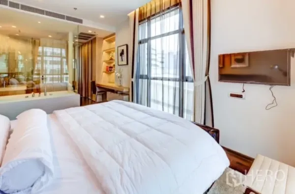 Condominium for rent or sale in Watthana, Bangkok - Bedroom with wall-mounted TV and expansive windows allowing natural light.