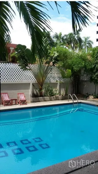 Condominium for rent in Khlong Toei, Bangkok - Outdoor swimming pool surrounded by palm trees with sun loungers on the deck.