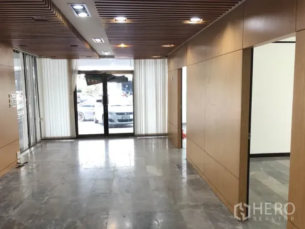 Home Office for rent in Huai Khwang, Bangkok - Ground-floor lobby with wood wall panels, marble flooring, recessed ceiling lights and a glass entrance.